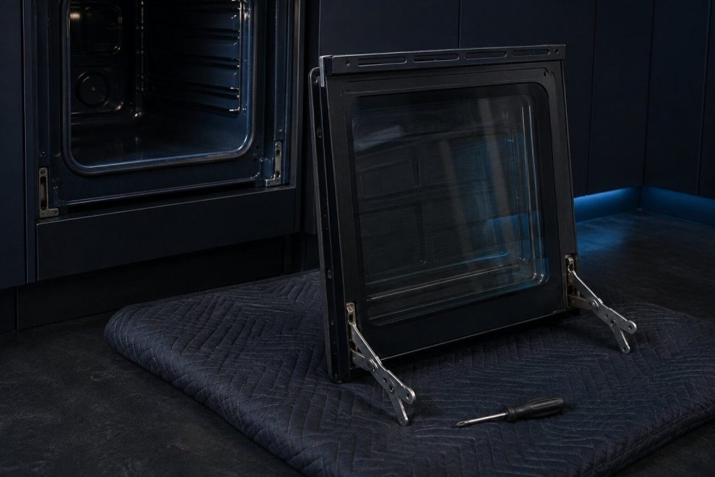An oven door lifted off and stood against a padded blanket, both hinge arms locked open